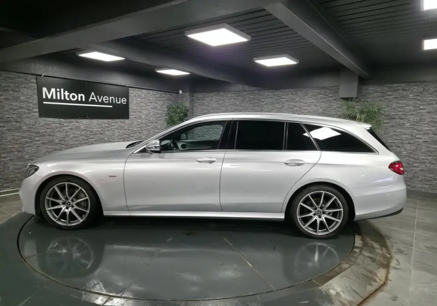 Vue latérale droite d'un break Mercedes Classe E gris métallisé avec jantes AMG 19 pouces dans un showroom intérieur.