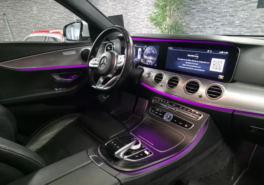 Vue intérieure côté conducteur du Mercedes Classe E Break gris, avec éclairage d'ambiance violet et écran large tactile.
