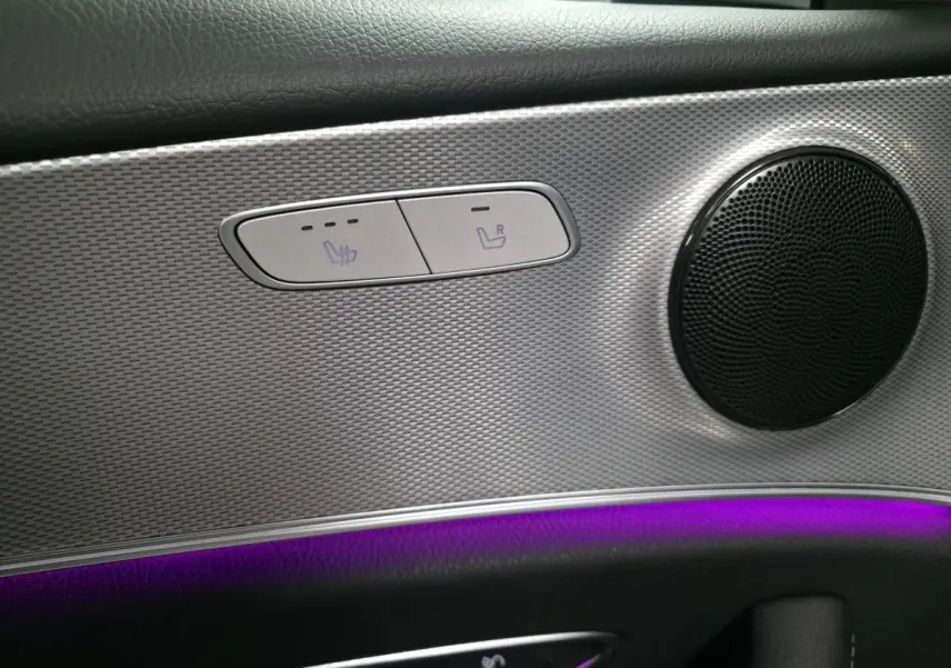 Détail du panneau de porte côté gauche avec haut-parleur rond, commandes de sièges chauffants et éclairage d'ambiance violet.