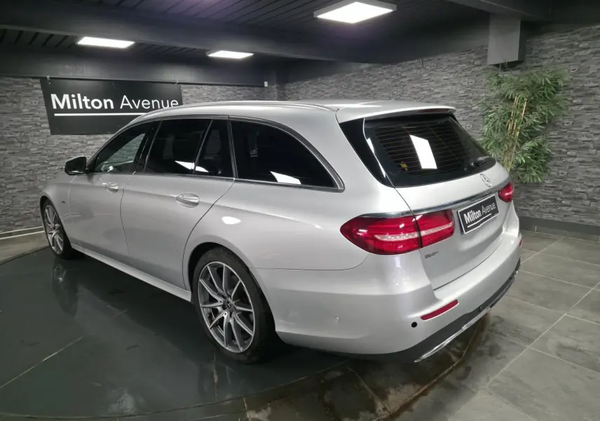 Vue 3/4 arrière droite d'un break Mercedes Classe E gris métallisé avec jantes AMG 19 pouces dans un showroom.