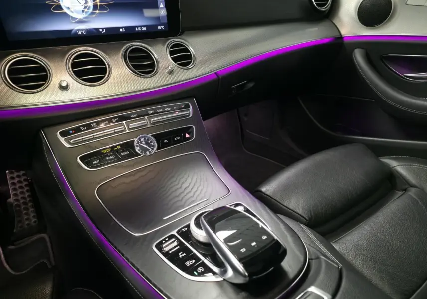 Vue intérieure côté passager du tableau de bord et console centrale noire avec éclairage d'ambiance violet sur Mercedes Classe E Break AMG Line 2020.
