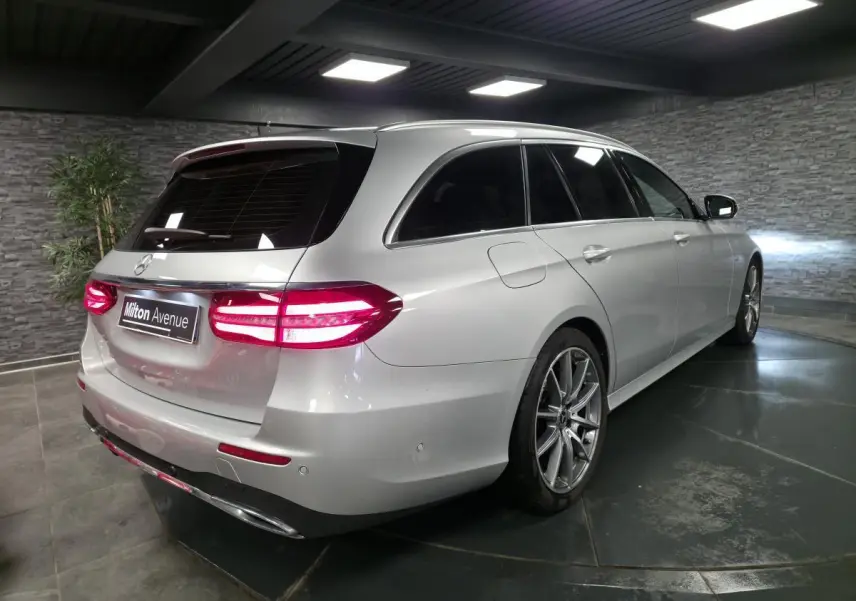 Vue 3/4 arrière droite d’un break Mercedes Classe E gris métallisé avec jantes AMG 19 pouces et vitres teintées.