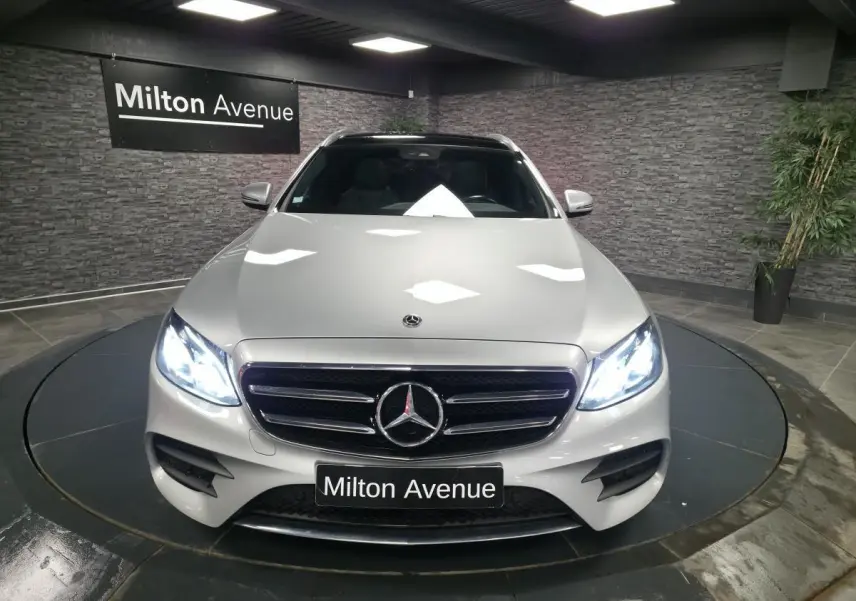 Vue avant d'une Mercedes Classe E Break E 200 d AMG Line gris métallisé avec phares LED allumés en intérieur.