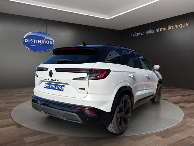 Vue 3/4 arrière droite du Renault Austral blanc avec toit noir, feux LED allongés et jantes noires en showroom.