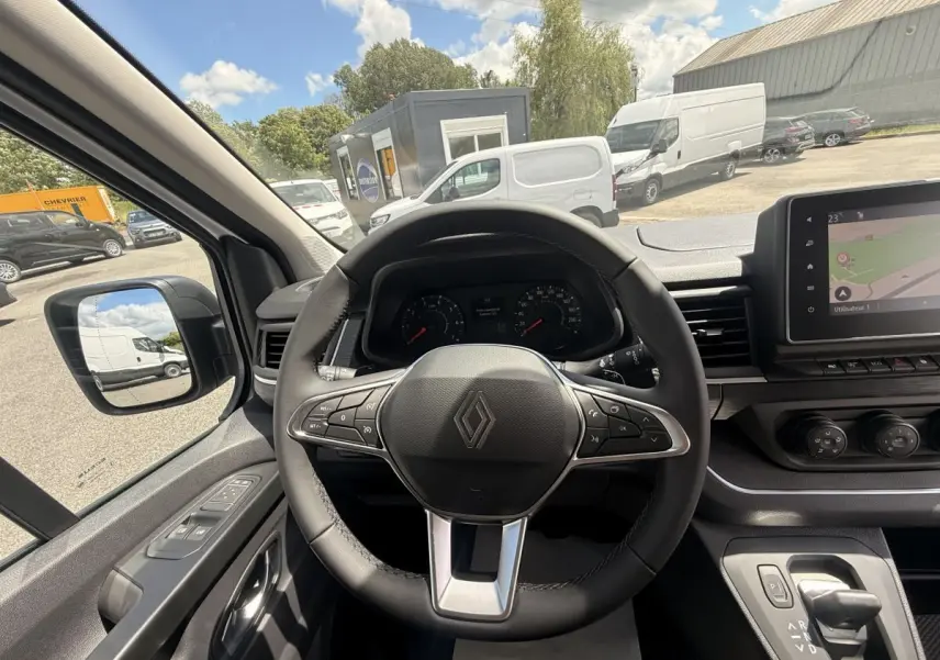 Vue intérieure centrée sur le volant multifonctions noir du Renault Trafic Fourgon blanc, avec tableau de bord et écran tactile visibles.