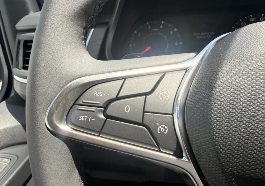 Gros plan sur les commandes du régulateur de vitesse au volant noir du Renault Trafic Fourgon blanc, vue côté gauche.