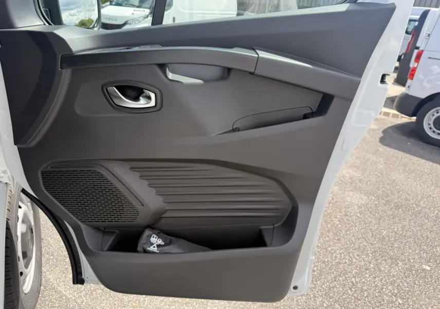 Vue rapprochée de la porte avant droite blanche du Renault Trafic Fourgon, montrant la poignée et le rangement intégré.