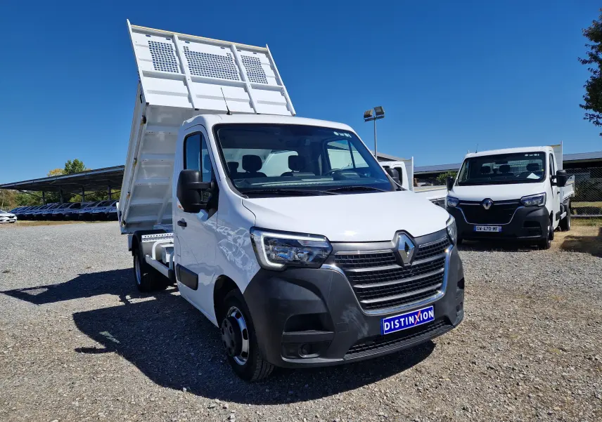Renault Master Benne blanc vue 3/4 avant droit avec benne relevée et roues jumelées sur sol gravillonné.