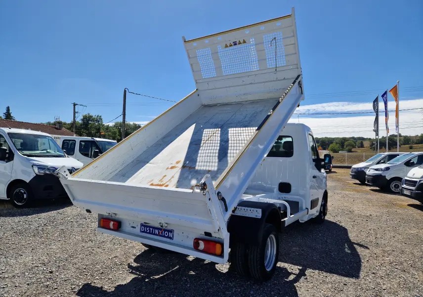 Vue 3/4 arrière droite du Renault Master Châssis Cabine blanc avec benne basculante relevée sur parking extérieur.