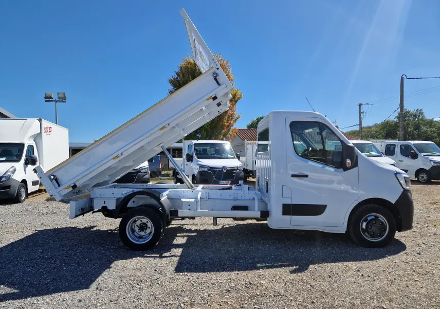 Vue de profil droit d’un Renault Master Châssis Cabine blanc avec benne basculante relevée sur un terrain extérieur.