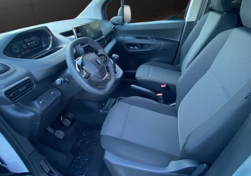Intérieur côté conducteur du Peugeot Partner 2024 blanc, avec tableau de bord moderne et sièges tissu gris noir.