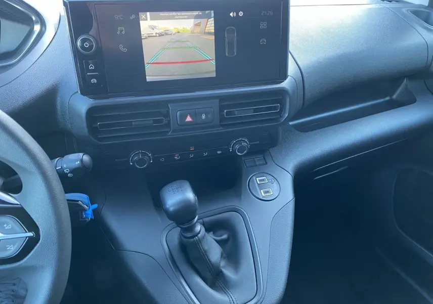 Vue intérieure du tableau de bord du Peugeot Partner blanc 2024, avec écran caméra de recul et levier de vitesses manuel.