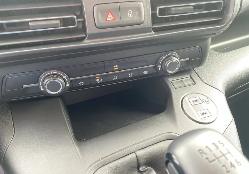 Vue rapprochée de la console centrale du Peugeot Partner blanc 2024, avec commandes climatisation et levier de vitesse manuel.