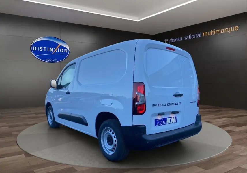 Vue 3/4 arrière droite du Peugeot Partner blanc, fourgon utilitaire avec logo et feux arrière visibles.