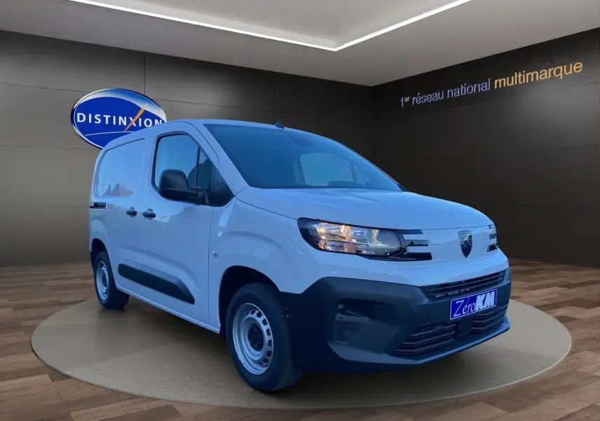 Peugeot Partner blanc en 3/4 avant droit, avec pare-chocs noir et jantes acier, en showroom intérieur.