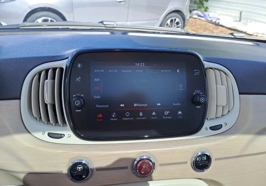 Tableau de bord clair de la Fiat 500 blanche, avec écran tactile central et aérateurs arrondis visibles de face.