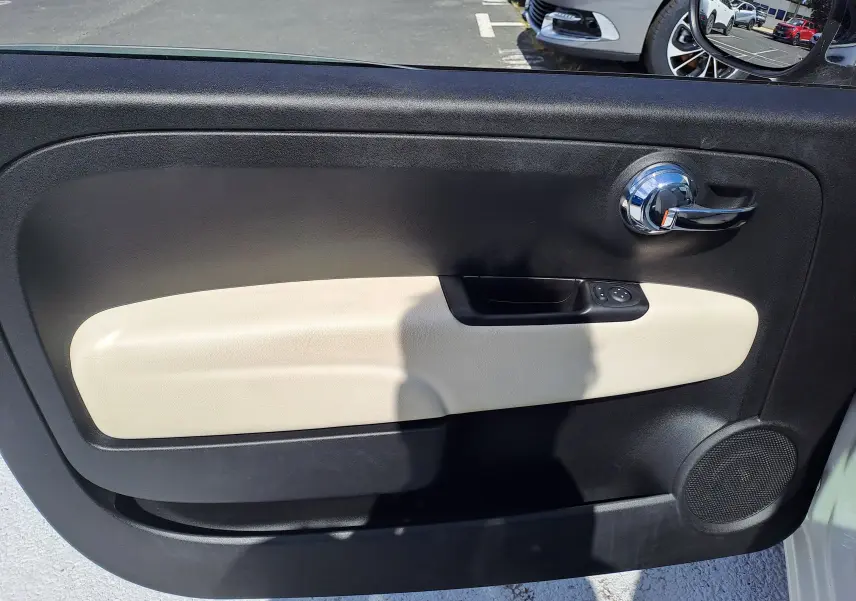 Vue intérieure de la porte côté gauche d'une Fiat 500 blanche, avec panneau noir et beige et poignée chromée.
