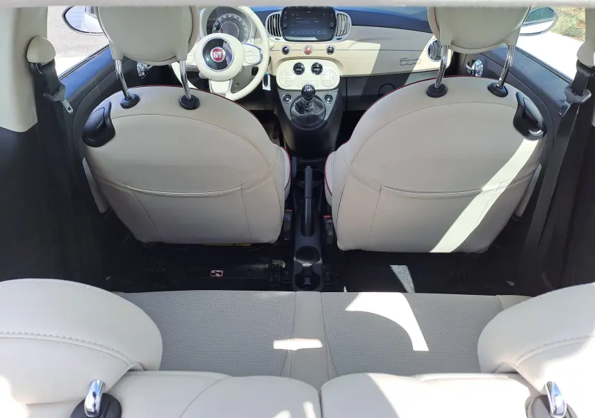Vue intérieure arrière du Fiat 500 blanc, mettant en valeur les sièges avant en cuir clair et le tableau de bord compact.
