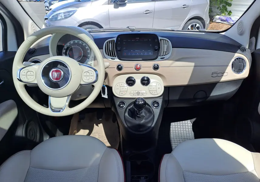 Vue intérieure avant de la Fiat 500 blanche 2022 avec tableau de bord beige clair et volant assorti.