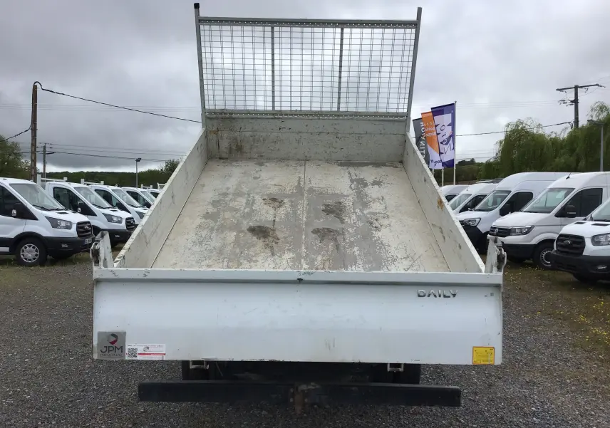 Vue arrière d'un Iveco Daily blanc avec benne basculante et grille de protection métallique.