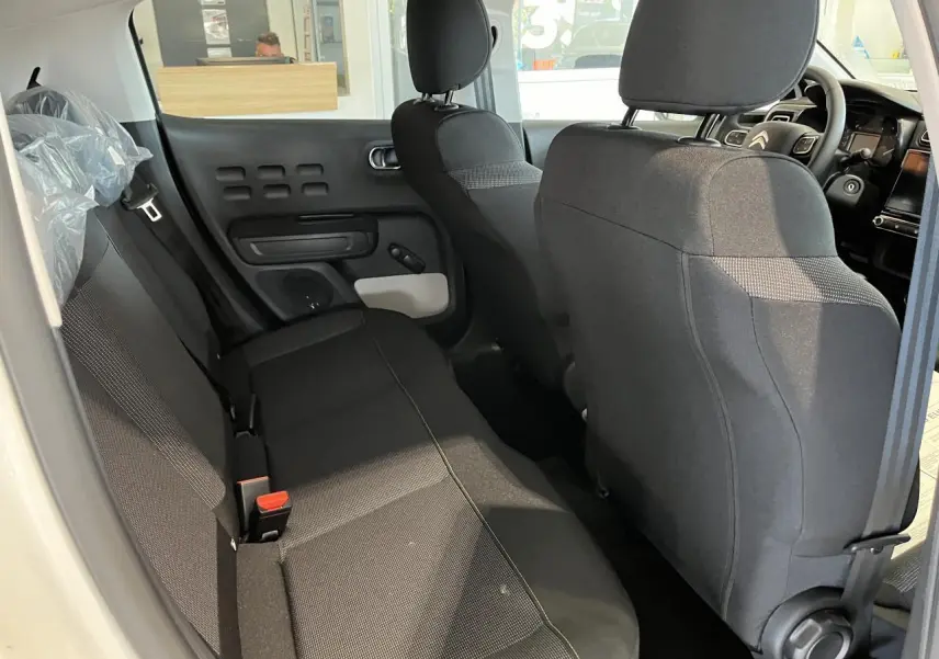 Vue intérieure arrière droite de la Citroën C3 blanche 2024, sièges tissu gris avec surpiqûres jaunes et accoudoirs textiles.