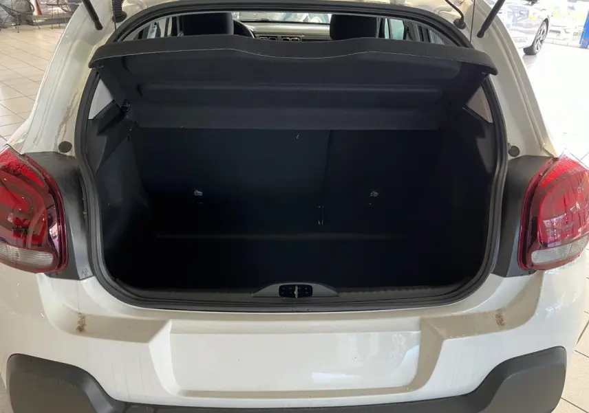 Coffre ouvert d'une Citroën C3 blanche vue de l'arrière, avec feux arrière rouges et pare-chocs noir mat.