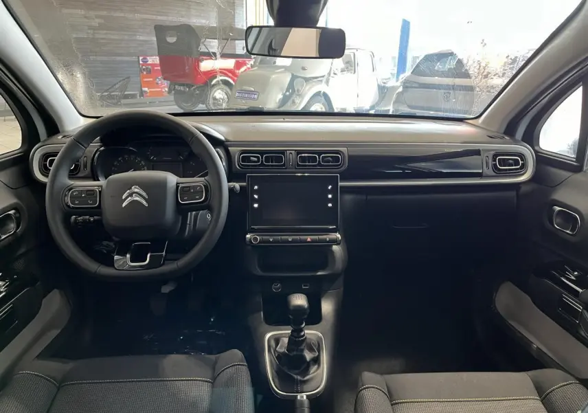 Intérieur de la Citroën C3 2024 vu de face, tableau de bord noir brillant avec écran tactile et volant multifonction.