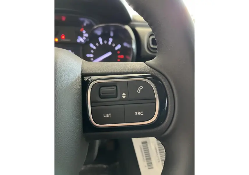 Gros plan sur les commandes audio au volant noir de la Citroën C3 2024, avec tableau de bord flou en arrière-plan.