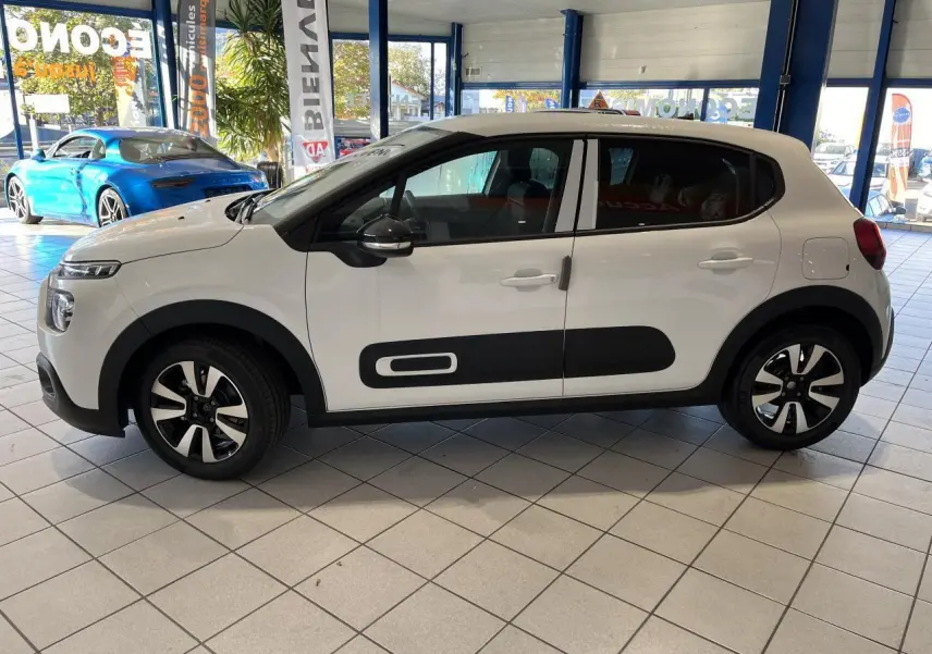 Profil droit d'une Citroën C3 blanche avec protections latérales noires et jantes alliage en showroom.