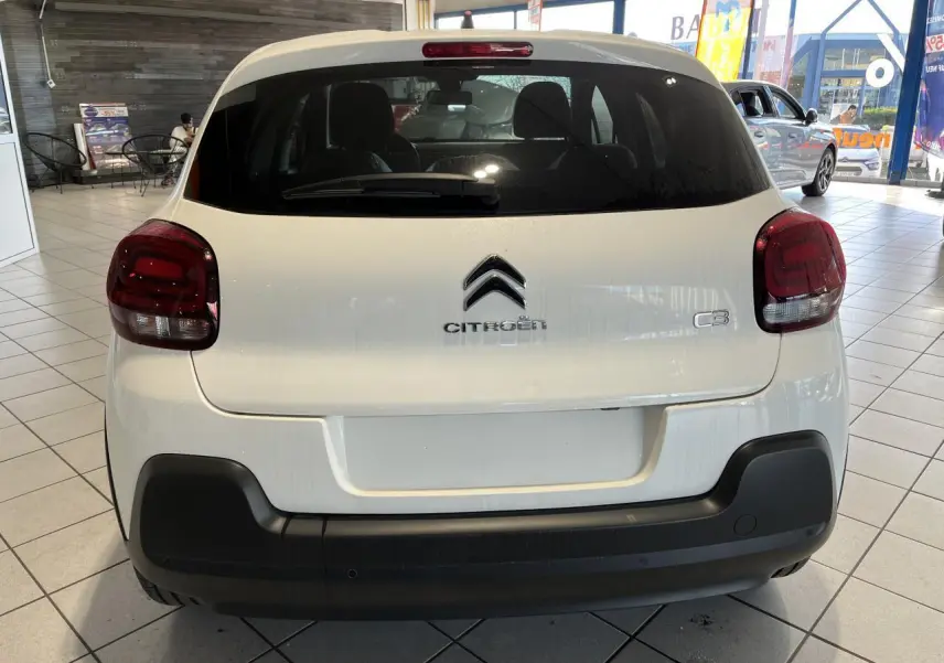 Vue arrière d'une Citroën C3 blanche avec feux arrière rouges et pare-chocs noir mat en showroom.