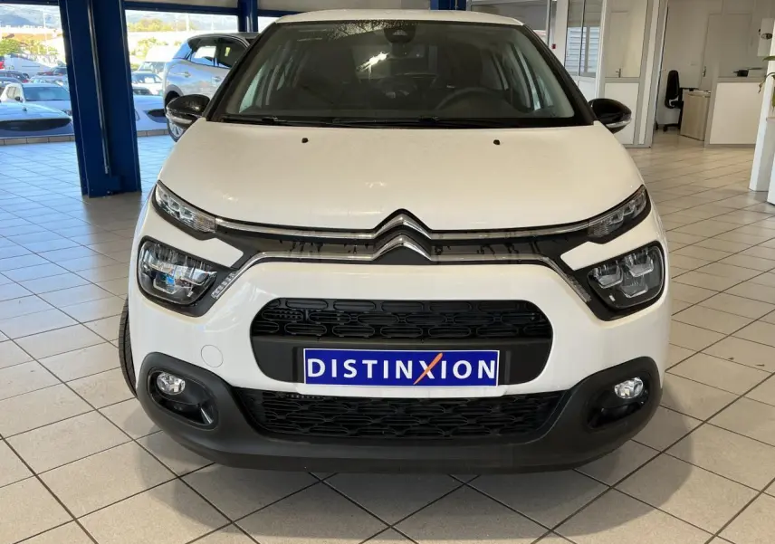 Vue frontale d'une Citroën C3 blanche avec calandre noire et feux LED dans un showroom lumineux.