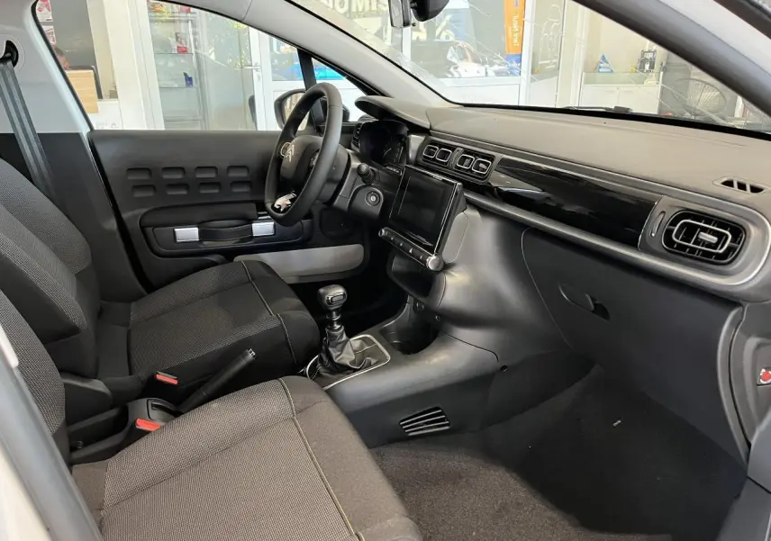 Intérieur avant droit de la Citroën C3 2024 avec tableau de bord noir brillant et sièges tissu gris foncé.
