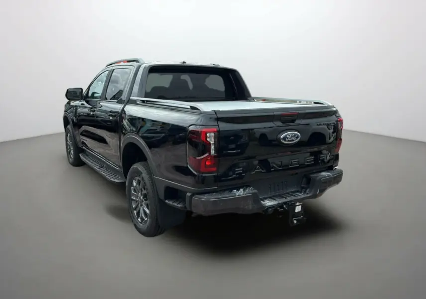 Ford Ranger 2025 noir agate vu en 3/4 arrière côté gauche, avec benne couverte et attelage visible.