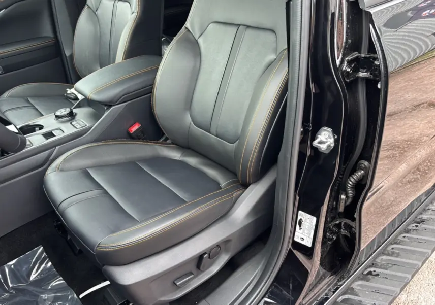 Vue intérieure côté conducteur du Ford Ranger 2025 noir agate, sièges cuir noirs avec surpiqûres orange et console centrale visible.