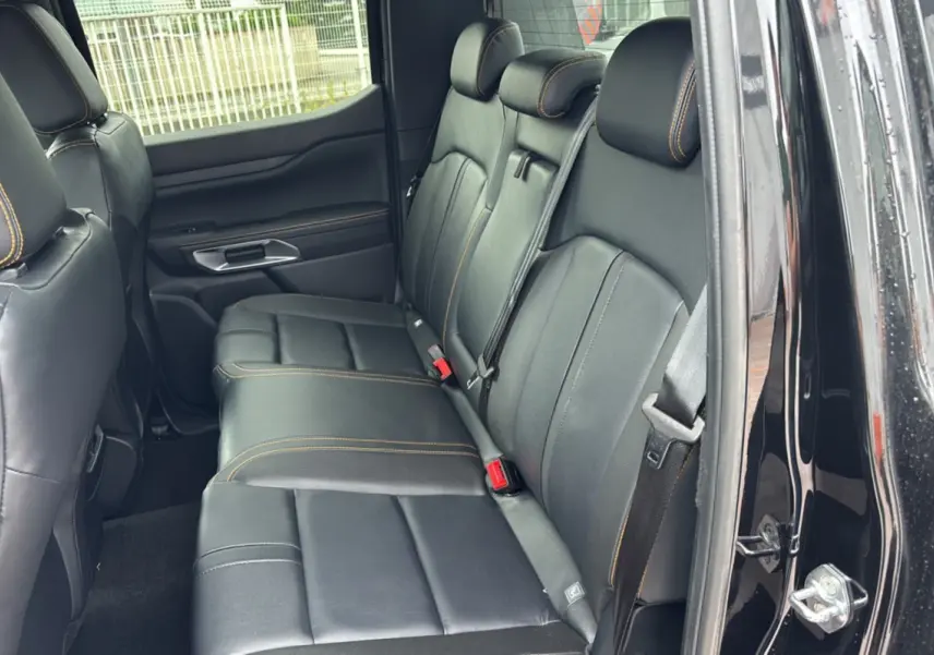 Vue intérieure arrière du Ford Ranger 2025 noir agate, sièges en cuir noir avec surpiqûres orange Wildtrak Plus.
