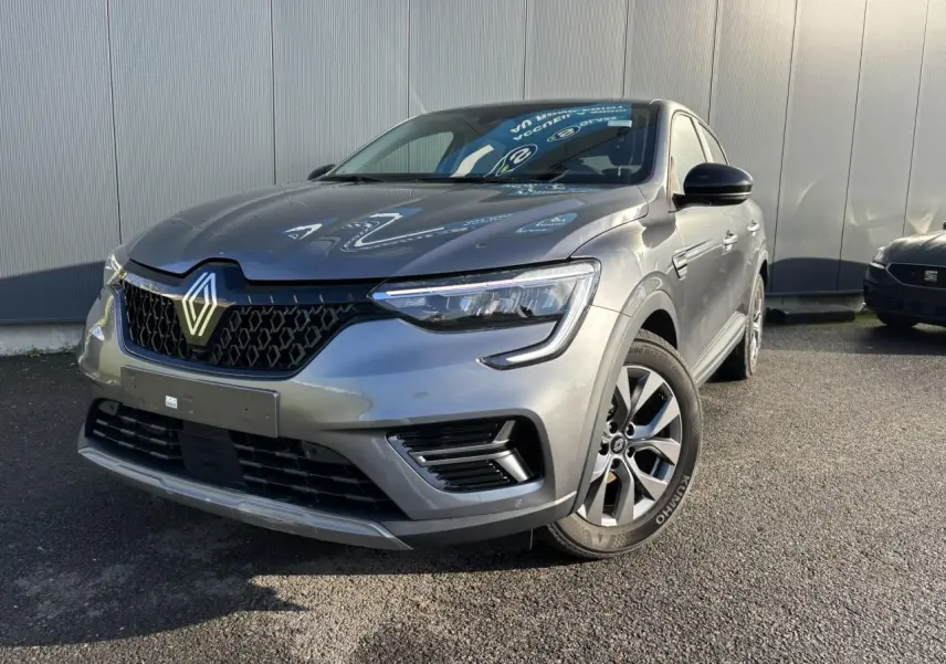 Vue 3/4 avant d’un Renault Arkana gris métallisé avec calandre noire et jantes alliage grises sur un sol asphalté.
