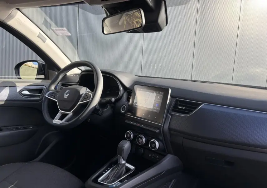 Vue intérieure côté conducteur du Renault Arkana gris métallique, mettant en valeur le volant, l'écran tactile GPS et la console centrale.