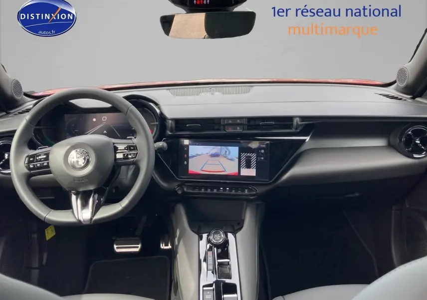 Vue intérieure frontale de l'Alfa Romeo Junior 1.2 hybride 2026, tableau de bord noir avec écran tactile et caméra de recul affichée.