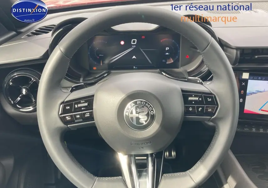 Vue centrée sur le volant noir de l'Alfa Romeo Junior 1.2 hybride 2026, avec tableau de bord numérique et écran tactile visible.