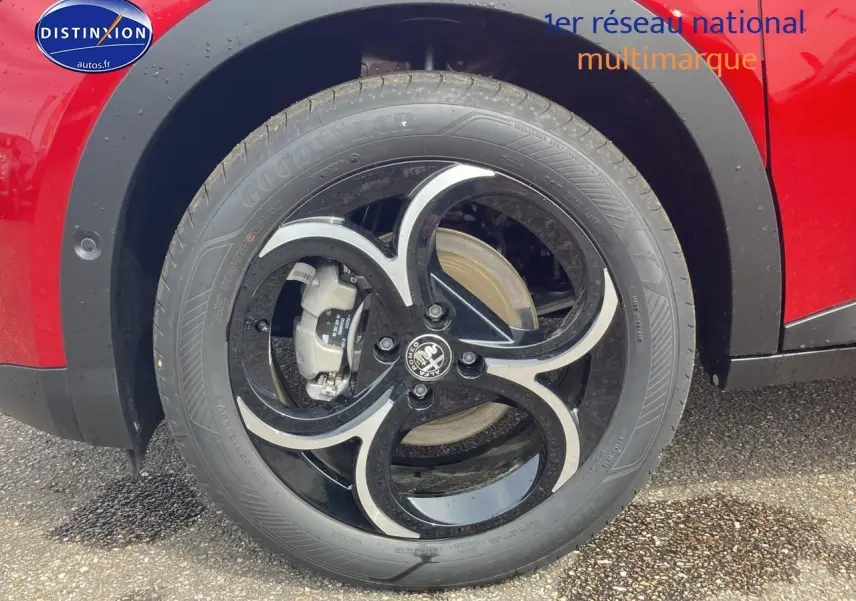 Gros plan sur la roue avant gauche d'une Alfa Romeo Junior 1.2 hybride rouge et noir, avec jante alliage noire et argentée.