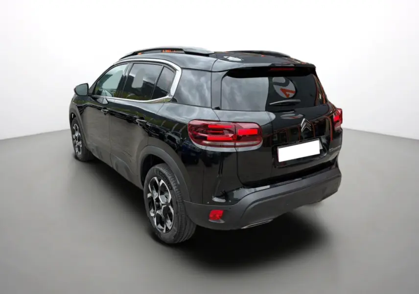 Vue 3/4 arrière gauche du SUV Citroën C5 Aircross noir métallisé avec barres de toit et jantes alu 18 pouces.
