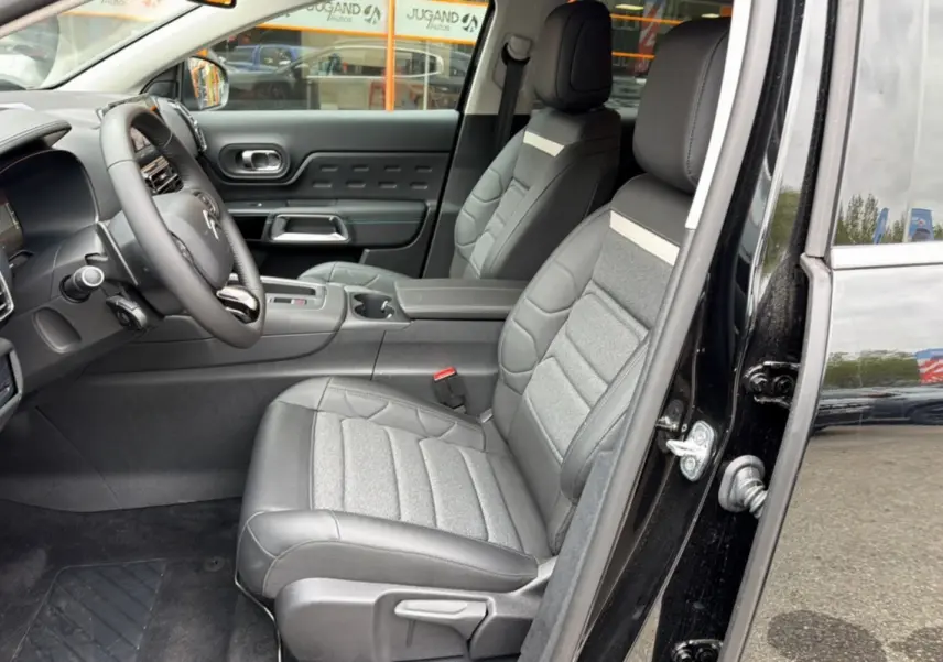 Vue intérieure côté conducteur d’un Citroën C5 Aircross noir 2025, sièges cuir et tissu gris avec console centrale et volant multifonctions.