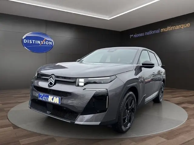 Vue 3/4 avant d'une Citroën C5 hybride gris foncé avec phares LED et jantes noires dans un showroom.