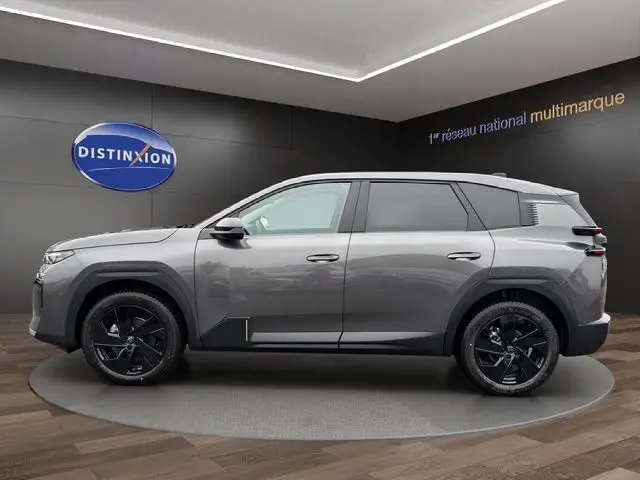Vue de profil côté gauche d'une Citroën C5 hybride gris foncé avec jantes noires en showroom.