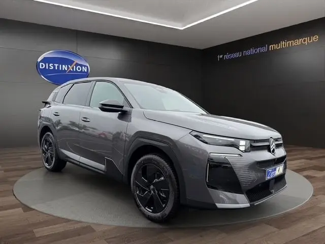 Vue 3/4 avant d'une Citroën C5 hybride gris foncé avec jantes noires, dans un showroom intérieur.
