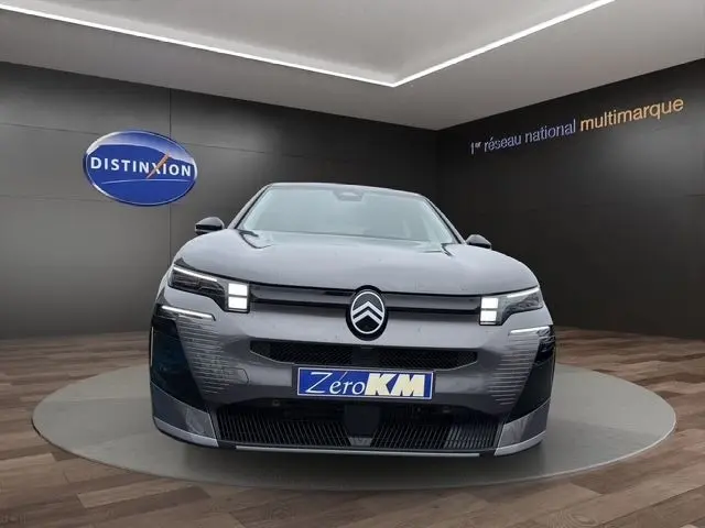 Vue frontale d'une Citroën C5 hybride gris foncé avec phares LED carrés et plaque "Zero KM" en showroom.
