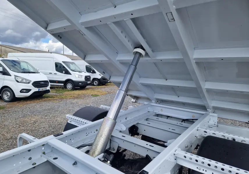 Vue rapprochée sous la benne relevée du Renault Master Châssis Cabine blanc, montrant le vérin hydraulique et le châssis.