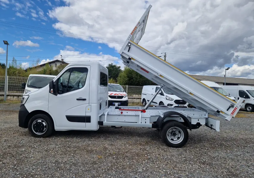 Renault Master blanc en vue de profil gauche avec benne relevée et roues jumelées arrière visibles.