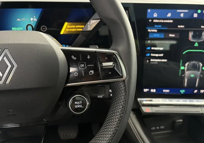 Gros plan sur le volant noir perforé du Renault Austral E-Tech avec commandes et écran tactile du tableau de bord visible.