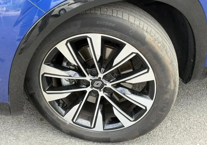 Gros plan sur la jante alliage 19 pouces diamantée noire du Renault Austral Bleu Iron, avec partie de l'aile avant visible.